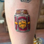Яркая татуировка банки варенья в стиле олд скул на икре, с надписью 'Jam' на этикетке.