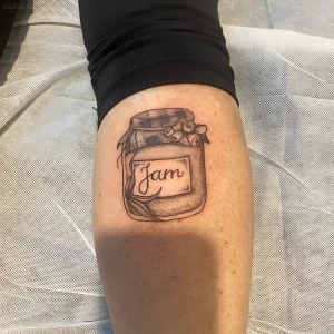 Черно-белая татуировка банки с вареньем на ноге, с надписью 'Jam'.