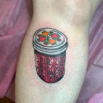 Яркая татуировка банки с красным вареньем, украшенной цветами, на ноге.