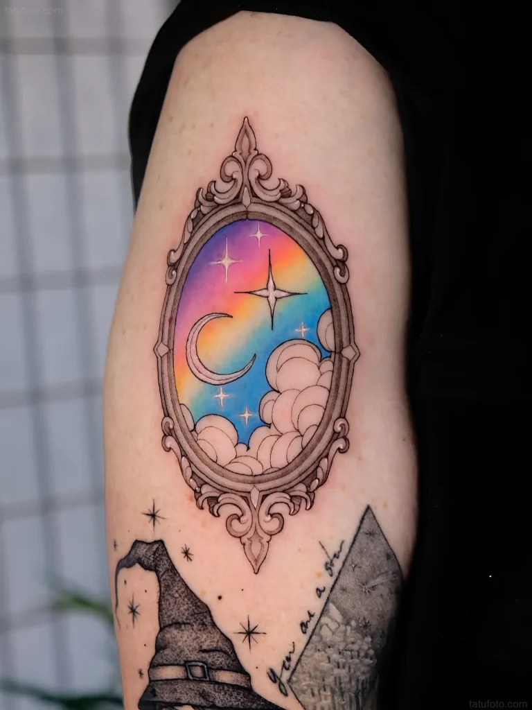 Tattoo of an antique mirror reflecting a magical night landscape with a rainbow sky, crescent moon, and shining star.