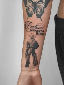 Черно-белая татуировка ковбоя со спины с надписью 'Fortune Favours The Bold' на предплечье