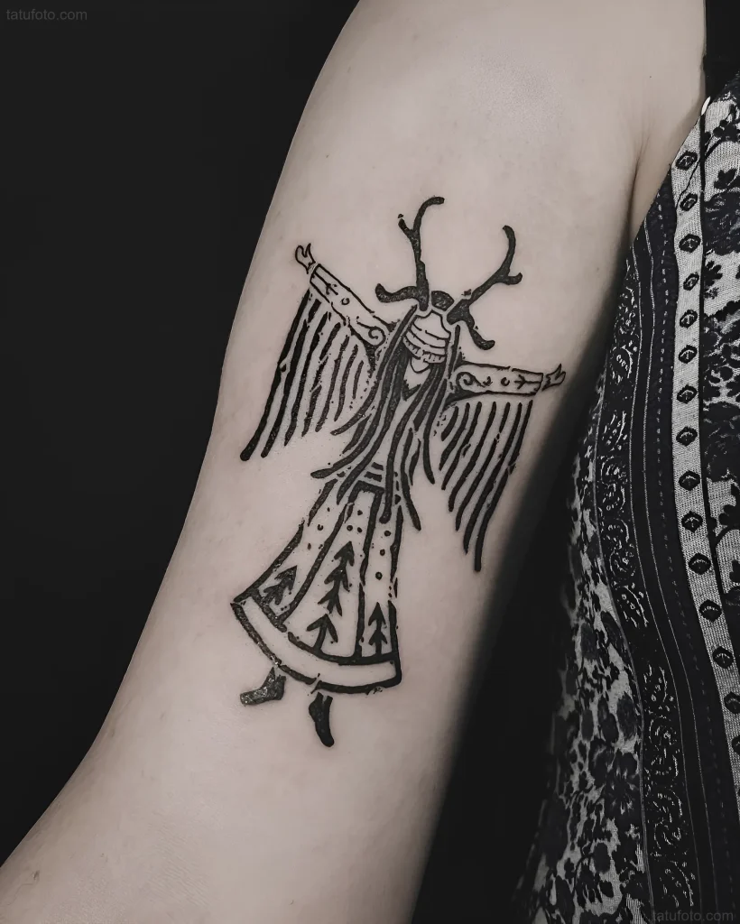 Tatuaje en blanco y negro de chamán con cuernos de reno y cabello largo, realizado en estilo gráfico en el antebrazo.