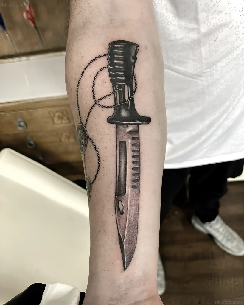 Tatouage réaliste de baïonnette avec une chaîne sur l'avant-bras