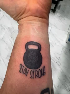 Татуировка гиря с надписью "STAY STRONG" на предплечье