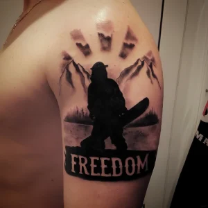 Силуэт сноубордиста с доской на фоне заснеженных гор и слова 'FREEDOM' на плече