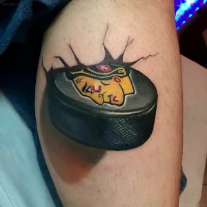 Татуировка хоккейной шайбы с логотипом команды Chicago Blackhawks, пробивающей кожу