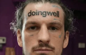 Крупный план мужского лица с татуировкой надписи «doingwell» на лбу.