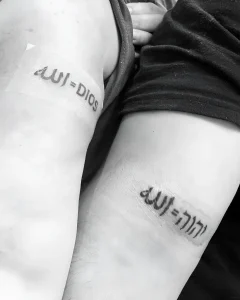 Черно-белое фото татуировки с арабским словом «Аллах» и латинским «Dios» на предплечье.
