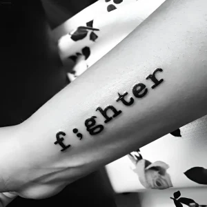 Черно-белое тату слова "fighter" с точкой с запятой вместо буквы "i" на предплечье