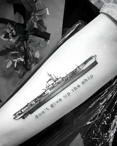 Черно-белая татуировка боевого корабля с надписью "don't give up the ship" на предплечье