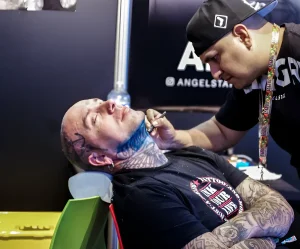 Тату-мастер работает над шеей клиента на выставке Mondial du Tatouage