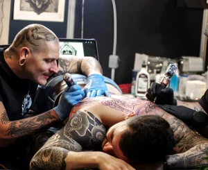 Мастер татуировки работает над спиной клиента на выставке Mondial du Tatouage в Париже.