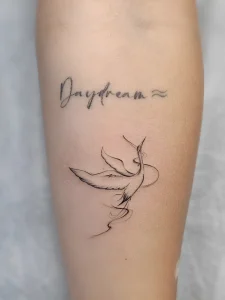 Минималистичная татуировка летящего журавля с надписью "Daydream" на предплечье