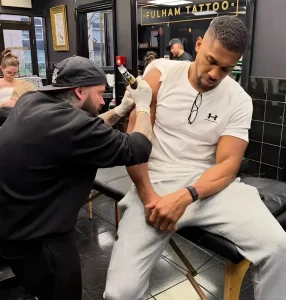 Энтони Джошуа делает татуировку на руке у мастера в студии Fulham Tattoo.