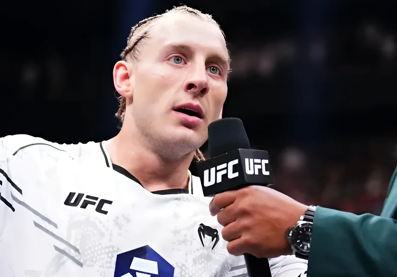 Боец UFC Пэдди Пимблетт дает интервью с микрофоном UFC, на нем белая футболка с логотипами UFC и Venum.