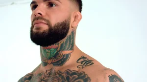 UFC боец Коди Гарбрандт крупным планом, демонстрирующий татуировки на шее и груди, включая бриллиант с крыльями и надписью 'MADE'.