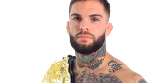 UFC боец Коди Гарбрандт крупным планом, показывающий свои татуировки на шее и груди, с чемпионским поясом на плече.