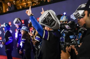 Группа фанатов Detroit Lions в тематических головных уборах и одежде, один из которых, Алекс Чепеска, демонстрирует головной убор с надписью "SUPER BOWL LIONS" и поднятым вверх пальцем.