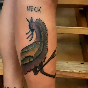 Татуировка эму с надписью 'HECK' на бедре