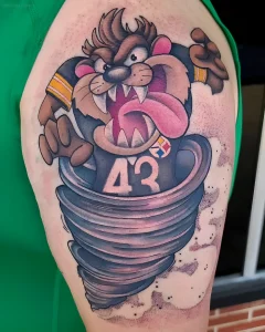 Татуировка тасманского дьявола в вихре, одетого в форму команды Pittsburgh Steelers с номером 43