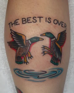 Татуировка двух уток, летящих над водой, с надписью "THE BEST IS OVER"