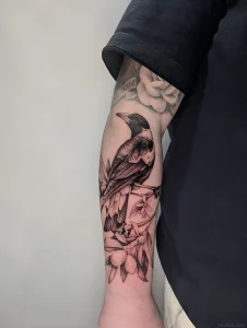 Татуировка сороки на руке, выполненная в стиле дотворк и графика, с изображением ветки с листьями и плодами.