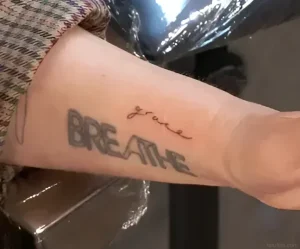 Крупный план руки Дрю Берримор с татуировкой слова «BREATHE» и слова «grace» над ней.