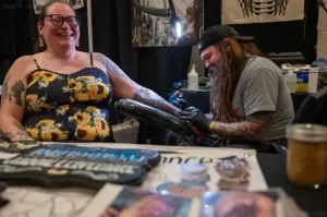 Художник Sideshow Brian делает татуировку на руке Кайла Уильямса на конвенте Electric City Tattoo Convention.