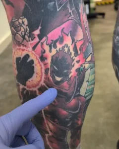 Крупный план ноги Тома Редфорда, покрытой яркими татуировками персонажей Marvel, включая огненного демона и каменных существ.