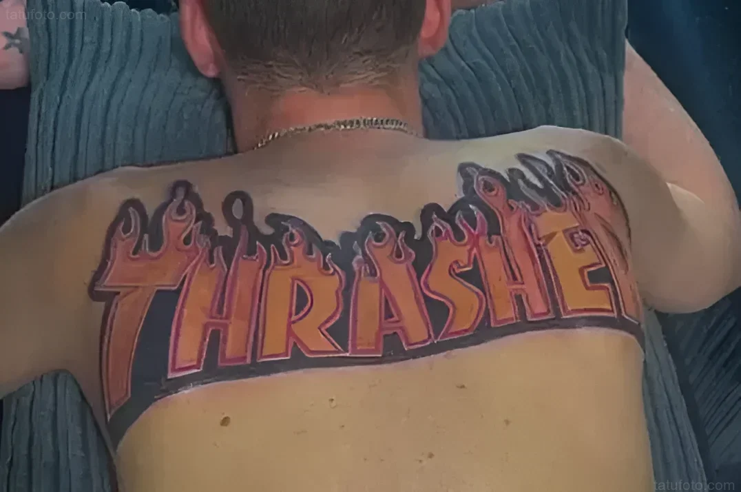 Крупный план спины мужчины с татуировкой логотипа Thrasher, выполненной в стиле огненных языков.