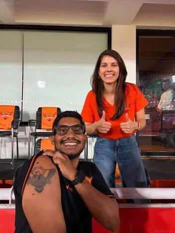Мужчина с татуировкой логотипа Sunrisers Hyderabad на плече и женщина, показывающая большой палец вверх, на трибуне стадиона