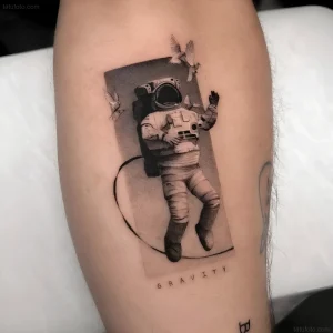 Татуировка космонавта в невесомости, окруженного птицами, с надписью "GRAVITY"