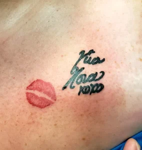 Татуировка в виде красного отпечатка губ и надписи "Kiss Me XOXO" черными чернилами