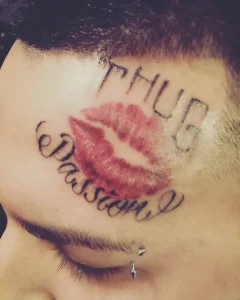 Татуировка с красным отпечатком губ и надписью "Passion" под словом "Thug" на виске