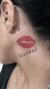 Татуировка в виде реалистичных красных губ и надписи "Blessed" в шрифте печатной машинки на шее.
