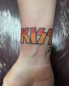 Татуировка буквы "KISS" в стиле рок-группы, выполненная в огненных оттенках на запястье.