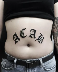 Татуировка ACAB, выполненная черными буквами в стиле готика на животе