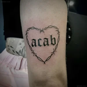 Татуировка ACAB внутри сердца, очерченного колючей проволокой, выполненная в готическом стиле.