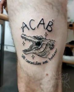 Татуировка ACAB с изображением аллигатора в стиле черной графики, нанесенная на бедро.
