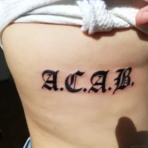 Татуировка ACAB, выполненная в готическом стиле на боку.