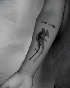 Татуировка акулы-молота с тенью и надписью "one life" на предплечье.