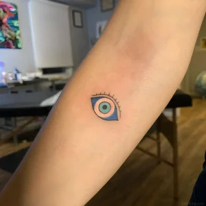 Миниатюрная татуировка "Глаз Фатимы" на предплечье, выполненная в контрастных цветах с четкими контурами.