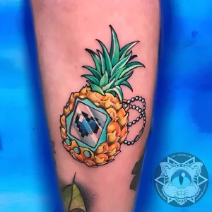 Татуировка ананаса, стилизованного под Digivice из мира Digimon, с пиксельным сердцем на экране и цепочкой.