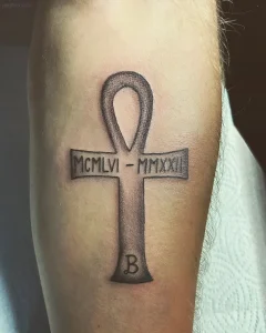 Татуировка Анкх с римскими цифрами MCMLVI - MMXXII и буквой B на предплечье