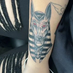 Татуировка Анубиса с красными глазами и анкхом на предплечье