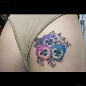 Татуировка анютины глазки в синих, фиолетовых и розовых оттенках на бедре