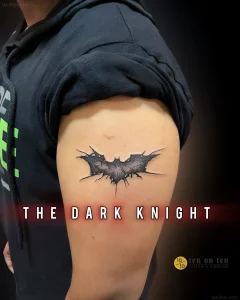 Татуировка Бэтмен в стиле реализм на плече, с надписью 'The Dark Knight' и эффектом свечения.