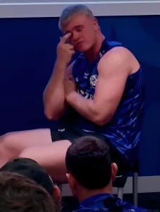 Игрок Canterbury Bulldogs Джек Андерхилл сидит на скамейке, задумчиво касаясь лба, рядом с ним товарищи по команде; на торсе видна татуировка с намеренно искажённым словом — символ памяти о матери