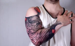 Детальная фотография татуировки на предплечье мужчины в стиле neo-traditional и blackwork, изображающая абстрактные формы, напоминающие волны или перья, с элементами красного цвета.