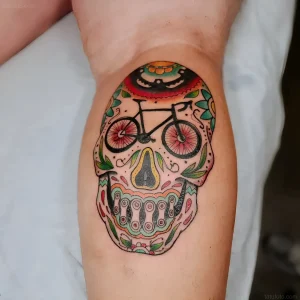 Цветная татуировка черепа с велосипедами на голени в стиле Sugar Skull